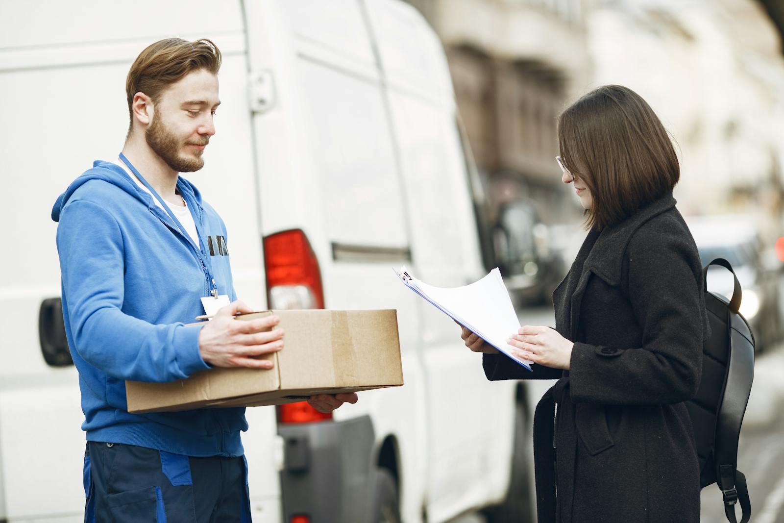 A courier hands over a package to a woman client on a city street, facilitating delivery service.